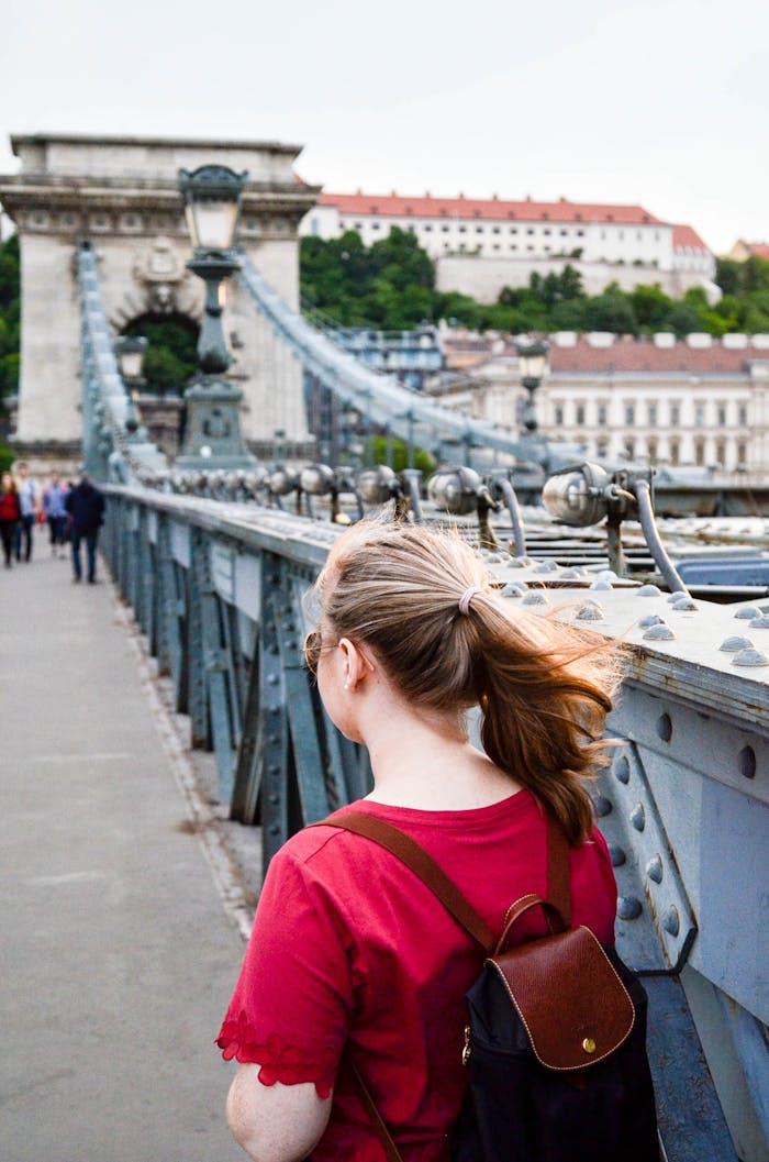 A woman with a backpack strolls the Széchenyi Chain Bridge in Budapest, enjoying a summer day.